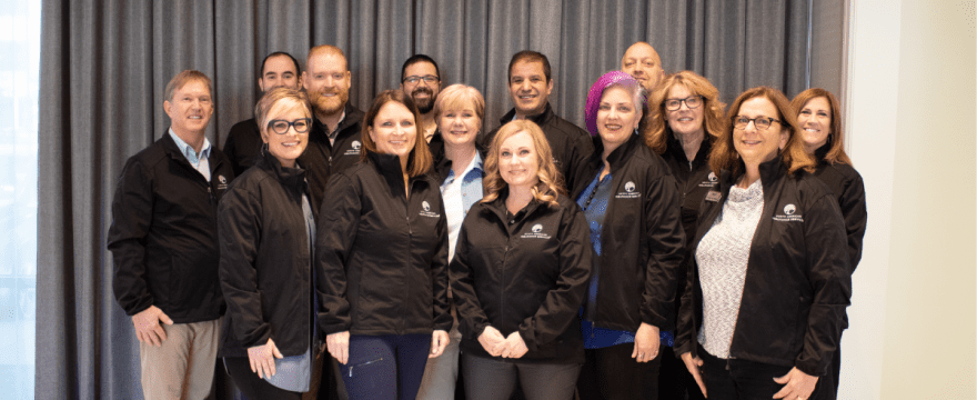 A group of insurance agents are standing together with matching black jackets with a North American Insurance Services logo smiling at the camera